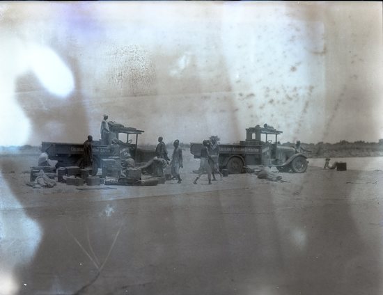 Hearst Museum object 1 of 2 titled Black and white negative, accession number 15-32377, described as 4" x 5" Negative. Expedition members unload the trucks at the edge of the Chari River.  Hoefler's original description: "French Congo. Unloading at the edge of the Chari River in order to cross on a small native ferry. It was plenty hot here and the sandy wastes extended for many miles behind and in front of us. It was always a mystery what lay ahead, but that is what made the effort worth while."