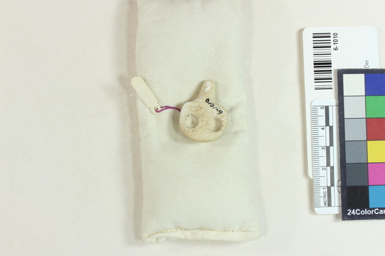 Hearst Museum object titled Amulet, accession number 6-1010, described as Limestone: amulet; eyes are 2 bored pits containing small limestone rings, set in with cement. Rounded back pierced by hole for string, behind eyes. Dynasty II.