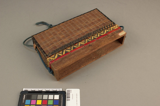 Hearst Museum object titled Basket, accession number 10-309, described as Basket; rattan, bamboo, wood; blue carrying cord; bottom brown; top natural; bands of red bamboo and yellow and brown decoration around top; oblong; 10 x  6 1/8 x 2 3/8”