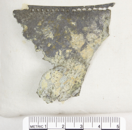 Hearst Museum object 16 of 45 titled Greaves, accession number 8-109, described as Bronze greave and 9 fragments small holes all around edge; serpent and scroll design raised and repousee; greave 41.9 cm long