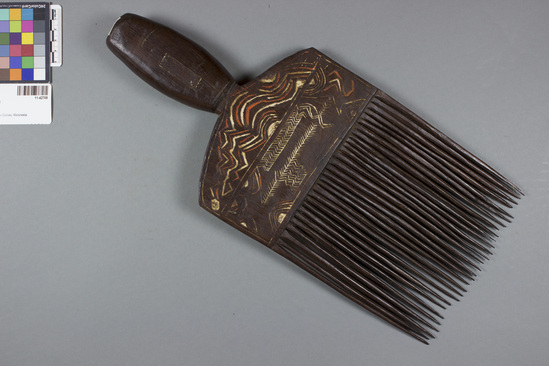 Hearst Museum object titled Wooden comb, pyro-graved and incised, accession number 11-42709, described as Comb, wood, pyro-engraved and incised, carved relief head on handle; 29 teeth; yellow, orange, white. length - 40.0 cm., width - 17.7 cm. Hair ornamentation.