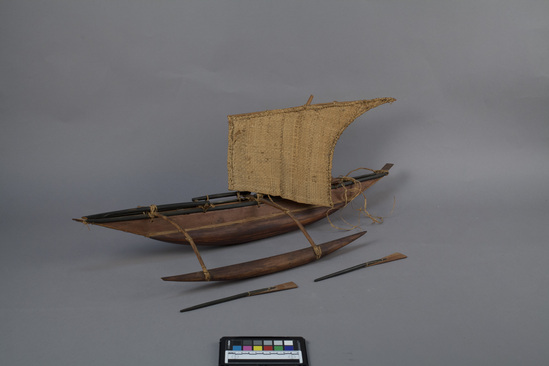 Hearst Museum object 5 of 5 titled Canoe model, accession number 11-42741a-c, described as Model of canoe, wood, single outrigger, single lateen sail, hull and sides laced together, 2 oars, undecorated. 71.0 cm.