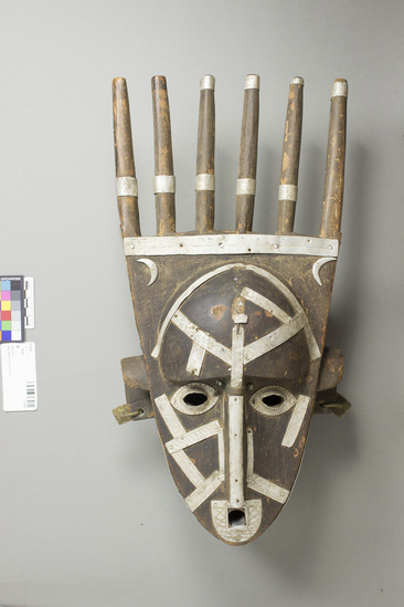 Hearst Museum object titled Mask, accession number 5-3339, described as Carved wooden face mask with a set of 6 parallel sticks on top. Strips of punctated tin used as decoration. Brass earrings. Ca. 18.5” x 9.0”