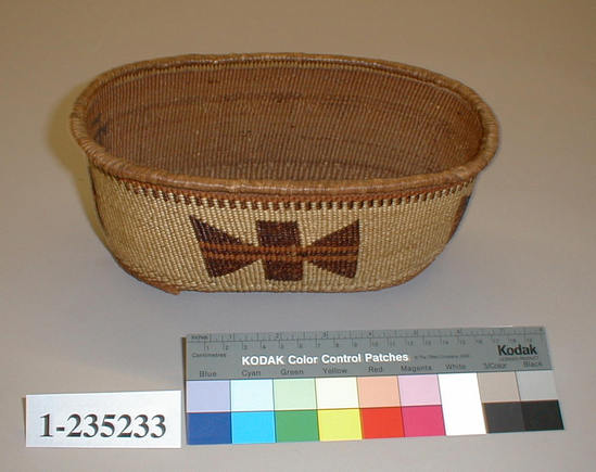 Hearst Museum object titled Basket, accession number 1-235233, described as Oval twined novelty basket with 4 bow - shaped designs in brown on straw - colored ground.  In ink on the interior of the basket are two swastika like symbols.  Tag "Kl. R. Tr. att.". Per Ralph Shanks:  Twined basket, made for sale.  Oval crossed warp starting knot. The warp material is probably hazel.  The basket has conifer root wefts.  The overlay weft material is beargrass, maidenhair fern, and red-dyed woodwardia.  Starting at the starting knot, there is plain twining to the edge of the base, where there are two weft rows of lattice twining. Going up the sides of the basket there are two weft rows of three strand twining, followed by plain twining up to below the rim where there is a single weft row of three strand twining followed by 1/8 inch of openwork parallel warps.  At the rim there are two weft rows of plain twining and a reinforcing rod wrapped with a peeled shoot.   The main design is four sets of butterfly-like figures that are formed by a central rectangle with two triangles.  The basket has a rightward work direction, with an up to the right slant of weft twist.  The overlay is single sided, with the design on the exterior.  The workface is on the exterior.  The basket is from Northwestern California.