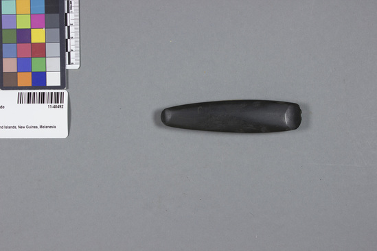 Hearst Museum object titled Blade, accession number 11-40492, described as Blade; dark gray stone; almost completely polished on both sides; long, narrow shape; length 11 cm. Wood working adze blade. Used for cutting out holes and grooves, as in the making of a canoe or a yam house or a house. Cutting edge ground on both ends, one of which is smaller than the other. Native name: ginesosu (attributed). Made of metamorphosed basalt.