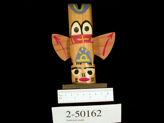 Hearst Museum object titled Totem pole model, accession number 2-50162, described as Miniature wood; plywood wings and base; painted faces, symbols; wings have red painted arrows.