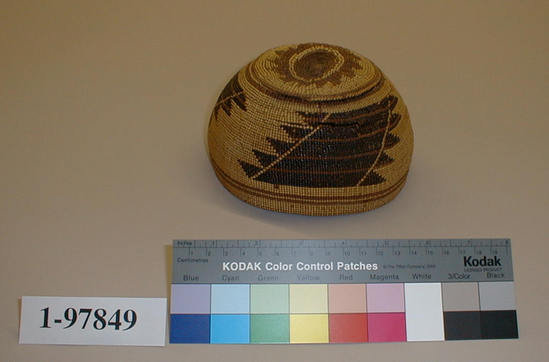 Hearst Museum object titled Cap, accession number 1-97849, described as Twined and cap like.  Black and brown design.  Tag "Klamath R. Tribes att.".  The hat has several breaks. Per Ralph Shanks:  Twined woman's basket hat.  Crossed warp starting knot, slightly indented.  The warp material is probably hazel. The weft material is conifer root.  The weft overlay background is beargrass with red-dyed woodwardia and maidenhair fern designs.  Starting at the starting knot, there is three strand twining for .5 inch, followed by 1.5 inches of plain twining, followed by one weft row of three strand twining.  Plain twining continues to .5 inch below the rim where there is one weft row of three strand twining.  The rim is trimmed.  The main design is three sets of five stacked parallelograms with two diagonal slashes throught them.  The basket has a rightward work direction, with an up to the right slant of weft twist.  The workface is on the exterior.  The overlay is single-sided, with the design on the exterior.  The basket is from Northwestern California.