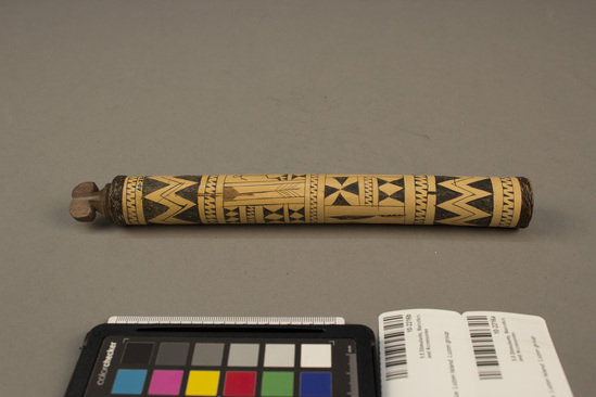 Hearst Museum object 3 of 3 titled Lime container and stopper, accession number 10-2216a,b, described as A) Bamboo lime container, decorated with incised geometric designs and stick figures; band of plaited rattan around one end; 8¾ inches long; B) wood stopper in shape of Bontre headdress.