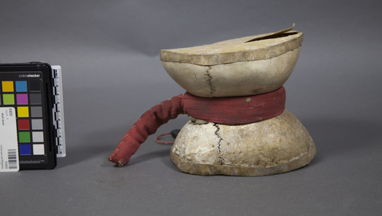 Hearst Museum object titled Skull drum, accession number 9-8252, described as Skull drum;2 top halves of human skull,covered w/hide w/tied red cloth; ht. 15 cm.