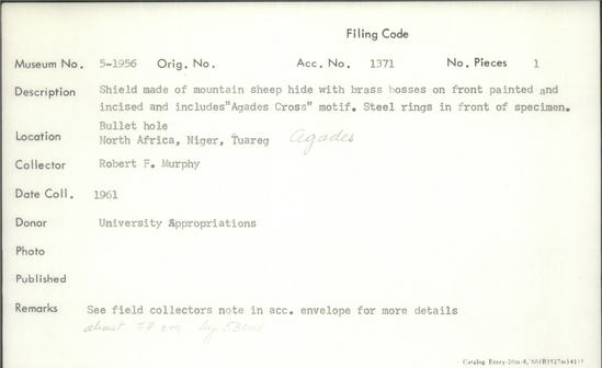 Documentation associated with Hearst Museum object titled Shield, accession number 5-1956, described as Shield made of mountain sheep hide with brass bosses on front; front painted and incised and includes "Agades Cross" motif; steel ring at top of specimen, and bullet hole is present in the specimen; length of shield is 69 ¾ inches.