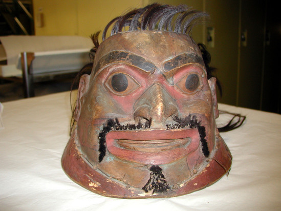 Hearst Museum object titled Helmet, accession number 2-19081, described as Wooden helmet, in form of head of a man, hair attached; painted red, black and blue. Label: "Fighting headdress and collar carving represents a worm, the same tradition as feast pipe.