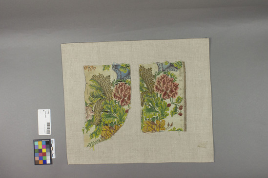 Hearst Museum object titled Textile sample, accession number 7-7428a,b, described as Two fragments made of silk, metal-wrapped yarns. Techniques: Jacquard, basketweave effect warp float ground. Colors: Grey ground, varicolored designs. Dimensions: a. 5 1/4 inches x 9 inches irregular b. 5 1/4 inches x 8 inches.