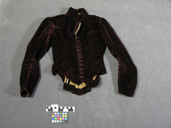 Hearst Museum object titled Jacket, accession number 2-66963, described as Maroon velvet woman’s jacket with tan cotton lining, fitted style with peplum and long sleeves. The velvet is worn and the buttons are missing.