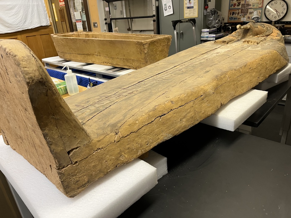 Hearst Museum object 128 of 167 titled Coffin, accession number 6-19912, described as Wooden anthropoid coffin. Inscription running down center of lid. Determined by Kea Johnston to probably be the outer coffin of Iwefaa (6-19928, 12-11039). According to Kea Johnston, "This coffin belonged to a man named Iwefaa, whose name is inserted in the middle of the spells written in the two columns on the front. This coffin is likely the outer coffin for PAHMA 6-19928 based on the similarity of the owner's name, unusual costume, and the paleography of the inscription. Both coffins were purchased on the antiquities market by George Reisner for Phoebe A Hearst. However, stylistically, they are very similar to a set of coffins known to have come from the site of Akhmim, which was excavated in the 1880s by Gaston Maspero, and which has heavily looted for the antiquities market during this decade." "The pectoral vignette between the text and the collar shows the deceased standing before squatting baboon and is the source of our logo. The hieroglyph for 'sky' is above their heads, and the side borders are formed by a pyramid and the symbol for the West.