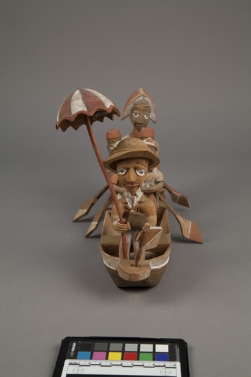 Hearst Museum object 6 of 15 titled Figures, accession number 5-16237a-q, described as caricature figure group; caricature of a District Officer on tour; carved & painted wood a - boat, has bag of frags b - Dist. officer (front) c - poler (rear) d - paddler (LF) e - paddler (LR) f - paddler (RF) g - paddler (RR) h - hat i - umbrella handle j - umbrella k - flag l - pipe m - pole n - paddle (RF) o - paddle (LF) p - paddle (LR) q - paddle (RR) Found two pegs in a bag with this object number.