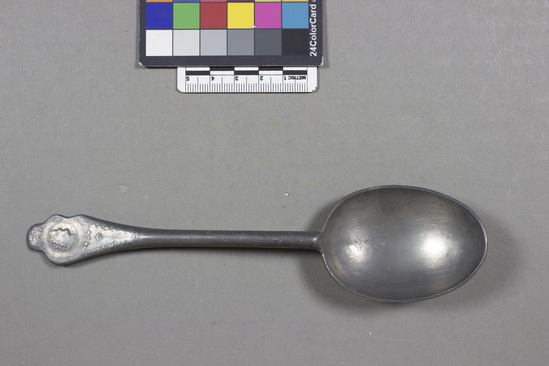 Hearst Museum object titled Spoon, accession number 7-2003, described as Spoon; pewter, cast; plover egg shaped bowl with rat tail handle; lobed handle end with women’s heads with circular frame relief; curvilinear design on rat-tail bowl back connection handle, back hallmarked with W; 7-1998-2007 are a set; length 18.5 cm.