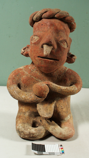 Hearst Museum object titled Figurine, accession number 3-3665, described as Red pottery effigy of seated man holding rattle