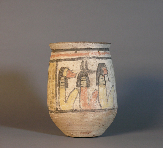 Hearst Museum object titled Ushabti jar, accession number 6-19835, described as pottery shabti jar with painted figures; the deceased (woman) kneels before Anubis, in form of a jackal on shrine.  3 of 4 sons of Horus: Hapy, Duamutef and Imseti on other side.