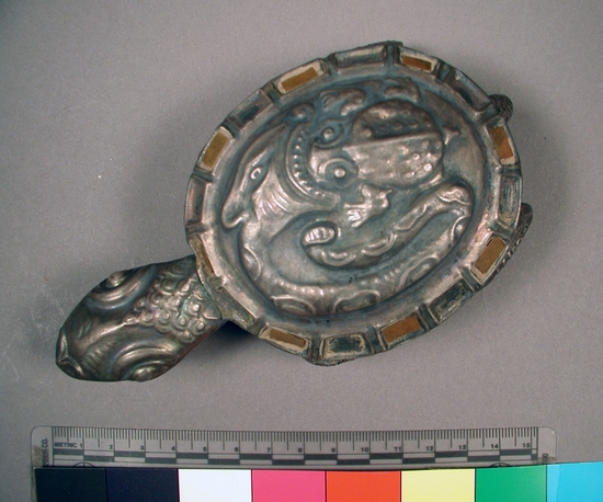 Hearst Museum object titled Turtle figurine, accession number 16-20440, described as Chimu style turtle constructed of shell metal. back of shell has motif of snake preparing to swallow a toad. inlays of red stone around shell.