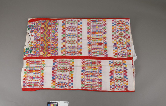 Hearst Museum object titled Huipil, accession number 3-17598, described as Huipil; White plain weave with multicolor weft brocade; some colored embroidery; elaborate patterns; 4 vertical red bands of ribbon on garment; w. at top 120 cm.