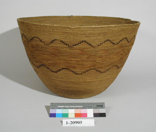 Hearst Museum object titled Bowl basket, accession number 1-20905, described as Large, deep, coiled. With one broad band in light brown, bordered by black serrations.  Tag on side bottom "Cahuilla" and on the bottom "No. 27[?] Property of Mrs. George H. Taylor Fresno, Cal." Per Ralph Shanks:  Coiled burden/storage basket.  Deergrass bundle foundation.  Weft designs are black dyed juncus and orange juncas. The background wefts appears to be tan juncus.  The design is a band of orange juncus surrounded  above and below by bands of black dyed juncus undulations.  One short line of black dyed juncus is at the side.  The basket has an interior workface with a rightward work direction.  The start is tightly woven.  The weft fag ends are bound under. The rim is plain wrapped with a herringbone ending, with the very end missing.  Based on the techniques, design, and materials,  this basket is from the Cahuilla.