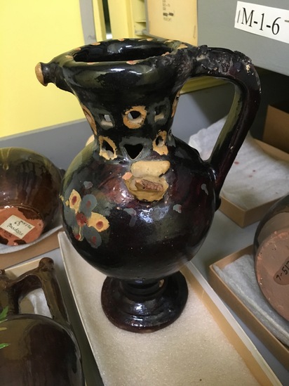 Hearst Museum object titled Trick wine jug, accession number 7-5153, described as Trick wine jug (grne vinsko - "wine jug"); pottery; spout in rim; single handle; brown glaze with yellow, grey, and red floral designs; holes in neck, 22 cm high