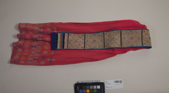 Hearst Museum object titled Sash fragment, accession number 9-23378, described as Sash fragment from woman's apron. Body of object made with pink cloth. Bottom 8" decorated with blue, yellow, green and white reversible cross stitch. Also embroidery. Bands of color. Strap covered in squares of 1mm wide appliqué patterns. Appliqué stripes at ends.