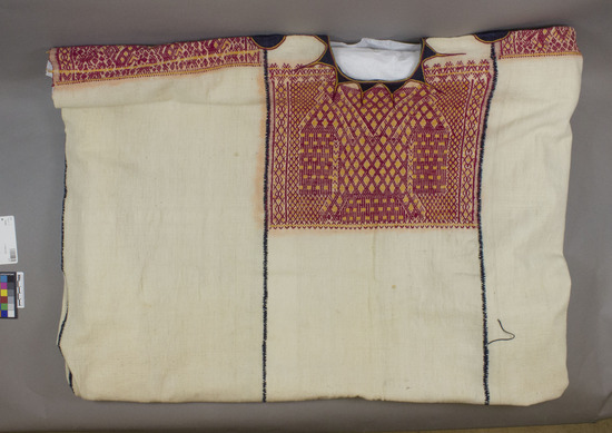 Hearst Museum object 3 of 3 titled Huipil, accession number 3-17, described as Woman’ shirt (huipil); white cotton; brocaded with red and yellow; stitched in dark blue; appliqued in dark blue ribbon; approximately 78 cm long, 96 cm wide For the color red the fiber is silk and the dye result is cochineal