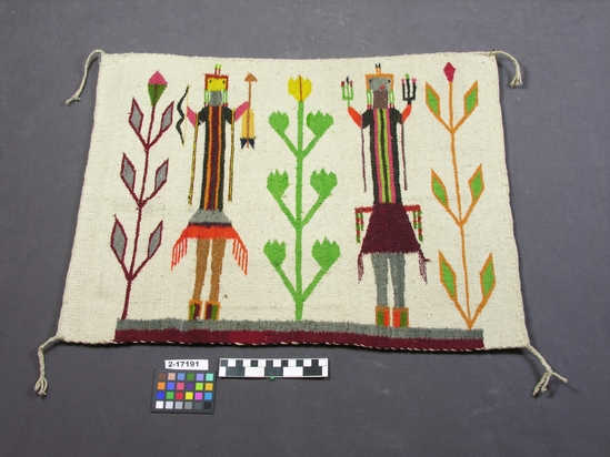 Hearst Museum object 1 of 2 titled Wall hanging, accession number 2-17191, described as Small, white blanket.  "Yei" throw with 2 figures, 3 corn plants; multicolor analine dyes on white ground.