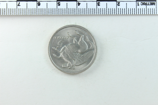 Hearst Museum object titled Coin, accession number 7-6117, described as Coin; bright; silvery metal; 5 drachmai; size: 25 mms. ; weight: 9.0250 grms.: mint condition Obverse: Pegasus flying, right; in field right, 5 ; below, N. (designer?) Reverse: Phoenix; below I. and date 1973; in field circling phoenix,