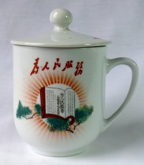 Hearst Museum object titled Mug and lid, accession number 9-23498a,b, described as The mug is decorated with a decal of an opened book resting on pine branches and radiating light, topped by the slogan: Serve the people (为人民服務 wei renmin fuwu) in imitation of Mao’s calligraphic script. The lid is almost flat with a round knob, a design that is typical of the mugs that Liling made for the CCP leaders and the Great Hall of the People; it bears an inscription. Inscription: Lid: “Smash the [four] olds; establish the [four] news” (破旧立新 pojiu lixin). For history of slogan see Helen Wang, Chairman Mao Badges, p. 143. Blue circular kiln mark on foot: “New Life Ceramic factory, Liling 1968” (醴陵新生瓷厂 Liling xinsheng cichang 1968)