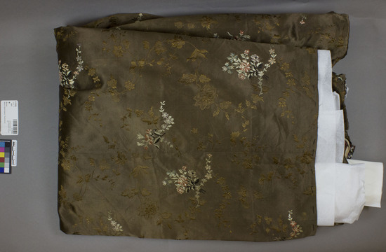 Hearst Museum object titled Skirt, accession number 3-11052b, described as Dress skirt; brown silk with brown silk floral brocade; varicolored silk floral embroidery.  Probably French 19th century fabric and tailored and embroidered in Mexico.