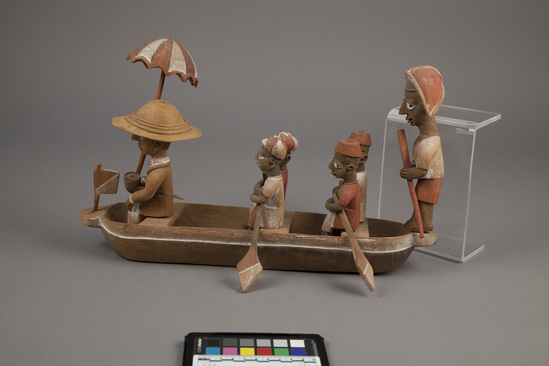 Hearst Museum object 8 of 15 titled Figures, accession number 5-16237a-q, described as caricature figure group; caricature of a District Officer on tour; carved & painted wood a - boat, has bag of frags b - Dist. officer (front) c - poler (rear) d - paddler (LF) e - paddler (LR) f - paddler (RF) g - paddler (RR) h - hat i - umbrella handle j - umbrella k - flag l - pipe m - pole n - paddle (RF) o - paddle (LF) p - paddle (LR) q - paddle (RR) Found two pegs in a bag with this object number.