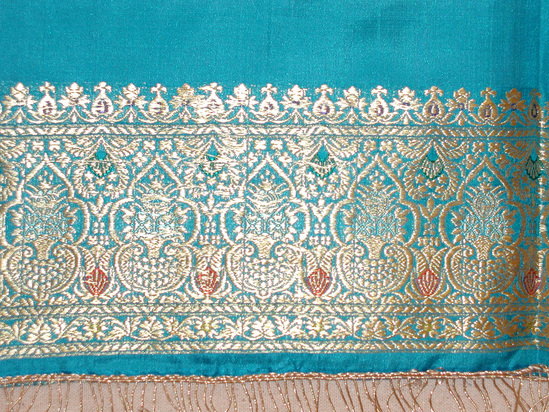 Hearst Museum object 2 of 2 titled Shawl, accession number 9-21536, described as Shawl;  turquoise-blue ground with predominantly “gold” metallic patterning, finely woven/. Turquoise warp and weft, plain weave, with narrow gold stripes at borders, and gold with purple, green, blue, orange, and yellow supplementary weft patterning; isolated floral motifs in discontinuous supplementary weft; ca. 2.3 cm border at each end in continuous supplementary weft; warp ends folded over and sewn down; fringe ca. 6.2 cm long, of gold-colored metallic thread looped through double row of twined gold-colored threads, sewn to each warp end.