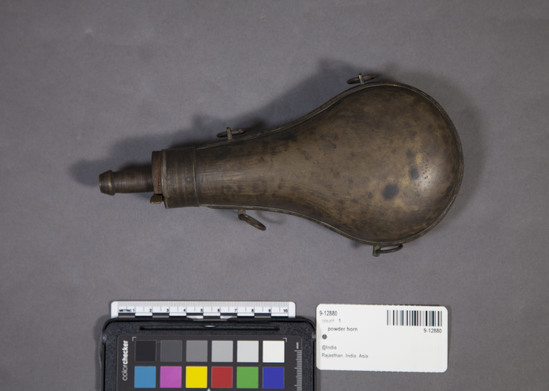 Hearst Museum object 3 of 4 titled Powder horn, accession number 9-12880, described as powder horn, brass; pear-shaped; external valve lever; 4 loops for hanging; l. 21.2 cm.