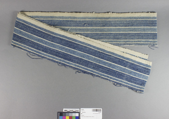 Hearst Museum object titled Garment, accession number 5-13022, described as Garment., Sierra Leone, Sherbro Mission, Sherbro attr. (possibly Mendi in origin) 1884. 5-13022, acc no. 3198. File code: 8.3 Collector: Rev. E.C. Lemmon through Rev. R. West. Donor: Mrs. Jane Erickson. Materials, techniques: Handspun cotton in plainweave; indigo dye Context of use: To be made into a garment of "country cloth" Description: Cloth strip; strip of indigo and white striped cotton cloth in plainweave; to be made into garment (cf. 5-13021); w. 11.5 cm., l. 1.96 M.