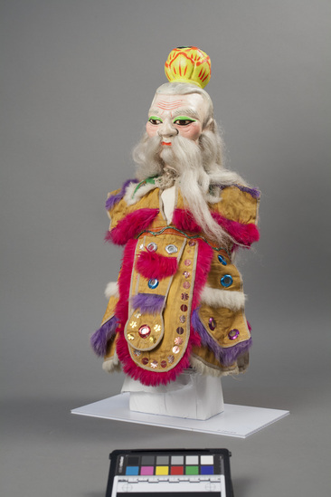 Hearst Museum object 1 of 8 titled Hand puppet, accession number 9-22424, described as Puppet, hand.  Taoist.  A.  Head:  carved wood, light pink, red mouth, green, brown and black features, painted gray hair,  long white hair, beard and moustache, yellow and orange lotus crown.  B. Body and legs:  cloth, white.  Hands:  wood, white, pink nails.  Boots:  wood, gray and white.  C. Robe:  cloth, yellow, green cape, gold, silver, red and blue mirrow, dark pink, white and purple rabbit fur trim.  49 x 24 cm (19 5/16 x 9 7/16 in)