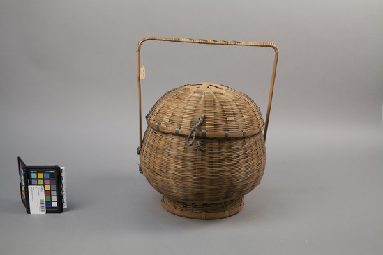 Hearst Museum object titled Basket and lid, accession number 9-12867a,b, described as basket; bamboo in wicker weave; round; has hinged lid with squared handle for carrying; a) basket with round base; height including handle 43 cm., b) hinged cover, diameter 29 cm. Some blue and blue-green decorative elements on both a) and b).