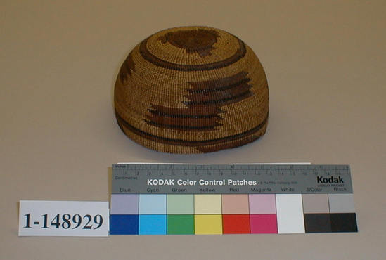 Hearst Museum object titled Cap, accession number 1-148929, described as Basketry hat with overlay; geometric design including parallelograms at rim.  Twined.  Tag "Klamath R. tribes att.". Per Ralph Shanks:  Twined woman's basket hat.  Crossed warp starting knot.  The warp material is probably willow or hazel.  The weft material is conifer root.  The weft overlay background is beargrass with designs in red-dyed woodwardia and maidenhair fern.  Starting at the starting knot, there is three strand twining for .5 inch, followed by 1 inch of plain twining, followed by one weft row of three strand twining.  Plain twining continues to .5 inch from the rim where there is one weft row of three strand twining.  The rim is trimmed.  The main design is three sets of two stacked parallelograms outlined in triangles.  The basket has a rightward work direction, with an up to the right slant of weft twist.  The workface is on the exterior.  The overlay is primarily single-sided, with the design on the exterior.  The basket is from Northwestern California.