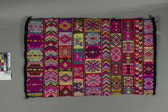 Hearst Museum object titled Textile, accession number 3-30374, described as sampler of embroidery designs.  ten vertical columns each containing a design in black, red, yellow, purple, pink, green, and ecru.  black borders on each end.  woven on back strap loom at Phoebe A. Hearst Museum by Martina Jiménez, Guatemalan weaver.