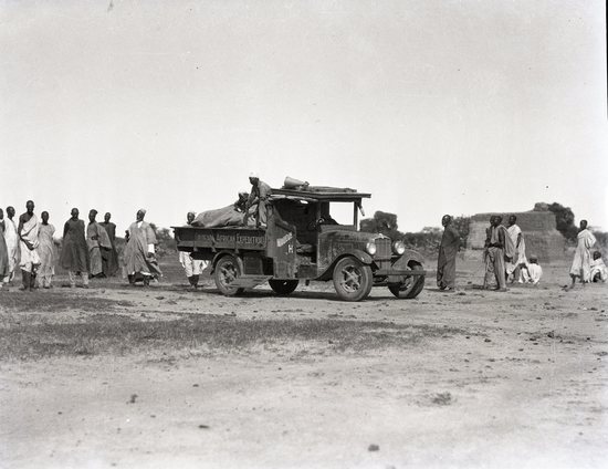 Hearst Museum object 2 of 2 titled Black and white negative, accession number 15-32378, described as 4" x 5" Negative. Truck in center with African peoples around it - preparing to cross Chari River.  Hoefler's original description: "French Congo. Crossing the Chari River."