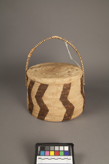 Hearst Museum object titled Basket, accession number 5-7201a,b, described as coiled basket w/lid, vertical brown zig zag designs. 33.5 cm height, 26 cm diameter. Native name: Manke from Dutch Mandje. Used for storage of rags etc. Collected 1968.