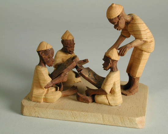 Hearst Museum object titled Thorn carving, accession number 5-11431, described as thorn carving;  represents a school scene;  teacher stands watching three sitting boys, who are writing their lessons on wax pallettes;  mounted upon soft wood base;  9.8 cm. x 9.6 cm x 8 cm