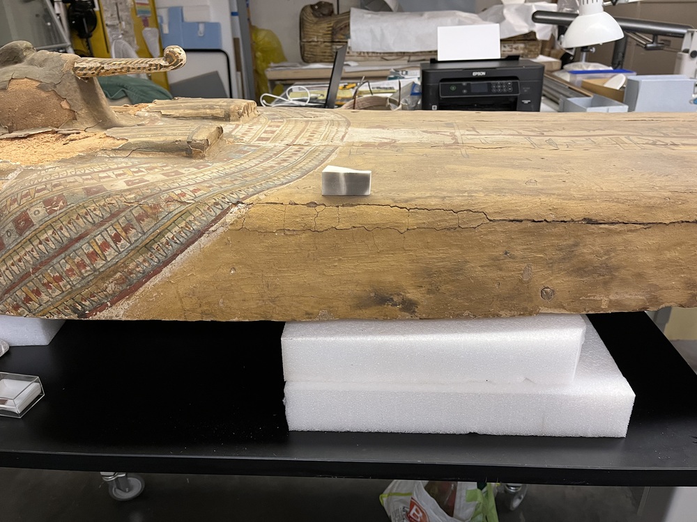 Hearst Museum object 92 of 167 titled Coffin, accession number 6-19912, described as Wooden anthropoid coffin. Inscription running down center of lid. Determined by Kea Johnston to probably be the outer coffin of Iwefaa (6-19928, 12-11039). According to Kea Johnston, "This coffin belonged to a man named Iwefaa, whose name is inserted in the middle of the spells written in the two columns on the front. This coffin is likely the outer coffin for PAHMA 6-19928 based on the similarity of the owner's name, unusual costume, and the paleography of the inscription. Both coffins were purchased on the antiquities market by George Reisner for Phoebe A Hearst. However, stylistically, they are very similar to a set of coffins known to have come from the site of Akhmim, which was excavated in the 1880s by Gaston Maspero, and which has heavily looted for the antiquities market during this decade." "The pectoral vignette between the text and the collar shows the deceased standing before squatting baboon and is the source of our logo. The hieroglyph for 'sky' is above their heads, and the side borders are formed by a pyramid and the symbol for the West.