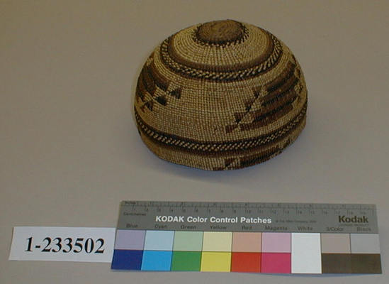 Hearst Museum object titled Basketry cap, accession number 1-233502, described as Twined basketry. Plain twining and 3-strand twining; pine root weft with overlay of Xerophyllum tenax leaf, maidenhair fern stem, and Woodwardia fern fiber. Designs in black and rust red on straw-colored ground. Hemispherical shape slightly peaked.