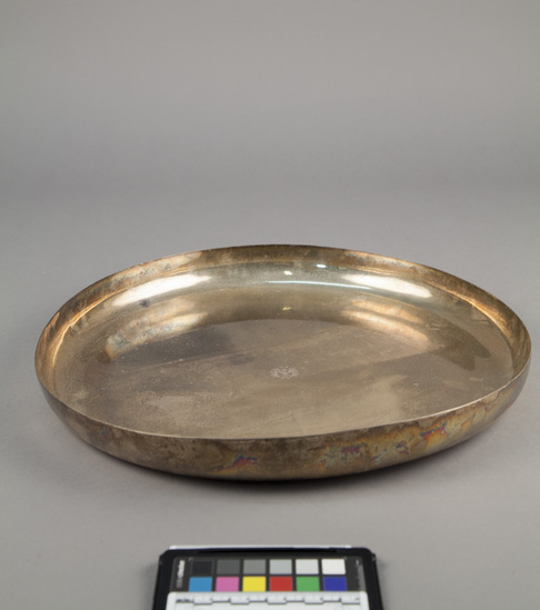 Hearst Museum object 1 of 3 titled Tray, accession number 9-12114, described as Ceremonial tray; Parsi; German silver, electroplated in silver; flat, circular bottom with slightly elliptical sides; owner’s initials in English on top center, donor’s father’s name in Gujerati on outer side, manufacturer’s trademark on bottom; used in religious and quasi-religious ceremonies to hold ceremonial objects or ritual and symbolic foods.  As with many Zoroastrian/Parsa ceremonial objects, it has a counterpart in common domestic use.