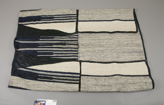 Hearst Museum object titled Robe, accession number 5-10129, described as Robe; sleeveless outer robe of white and indigo-dyed goat hair in weft face plain weave; alternating vertical stripes of indigo on white ground; black rayon panels with wavy machine-sewn stitches on inside edges of upper part of garment; black rayon tape trim; w. across shoulder 71 cm, l. 103 cm.