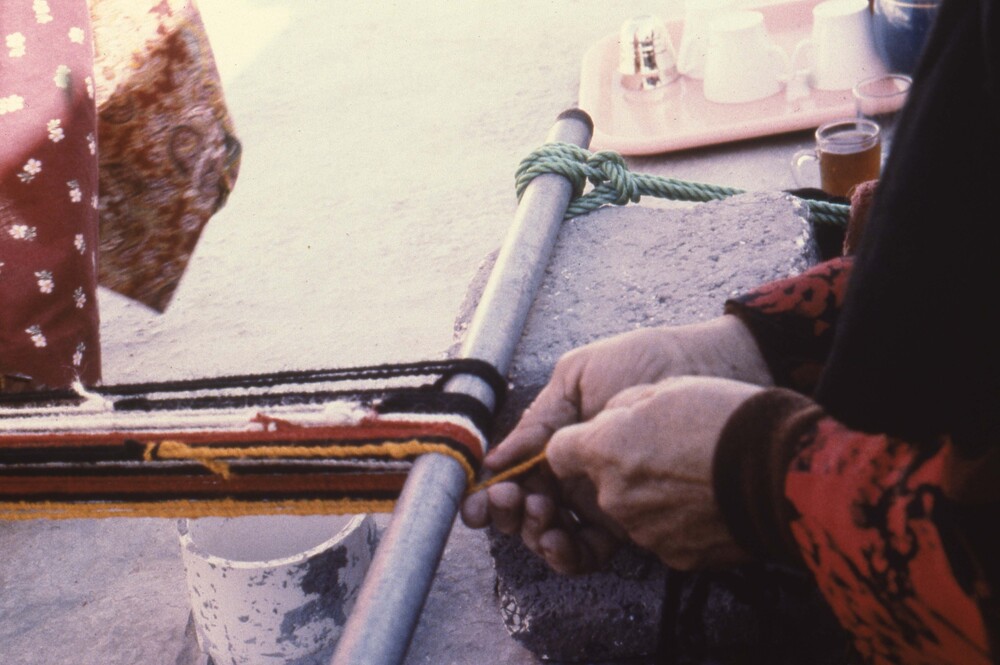 Hearst Museum object titled Color slide, accession number 25-98790, described as 35mm color slide transparency. Close-up of a person's hands weaving on a loom on the ground.