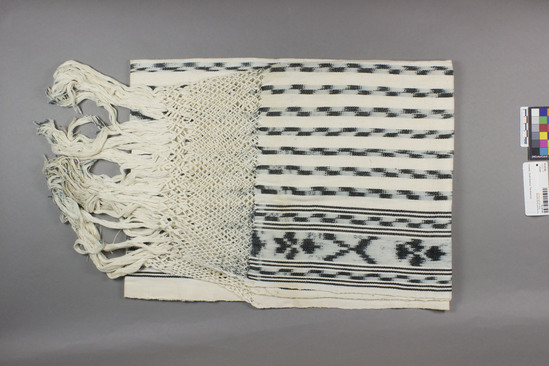 Hearst Museum object titled Shawl, accession number 16-20186, described as Shawl; 150 cm x 69 cm without the fringe; fringe . 35 cm, including 13 cm of macramé; white ground has 14 ikot indigo a stripes equally spaced apart; one stripe twice the width of the others, the two edges of the shawl have 10 cm bands of ikat and narrow plain indigo lines.