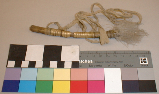 Hearst Museum object titled Whistle, accession number 1-1467, described as Bone, wrapped in natural colored fiber and cotton fabric; cotton strip attached near proximal end. Black mastic plug at distal end.